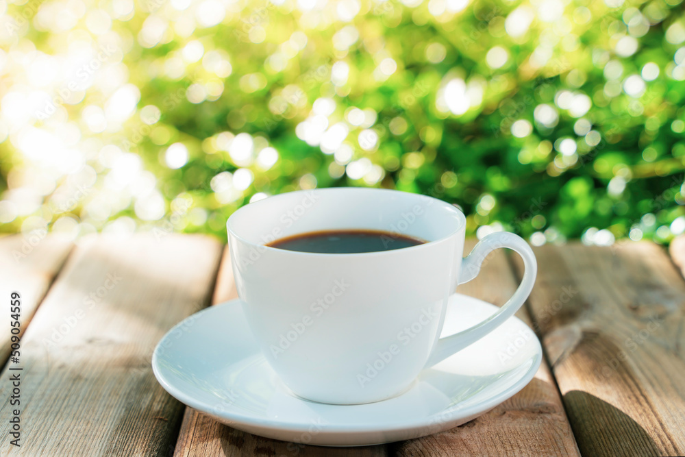 Fototapeta premium white ceramic coffee mug On the wooden floor, green tree bokeh background.