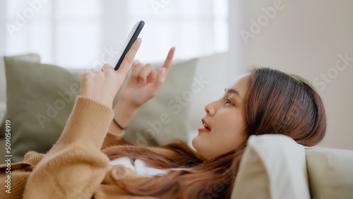 Billede på lærred Happy young asian woman relax on comfortable couch at home texting messaging on