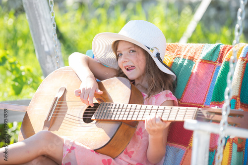 Little girl musician playing guitar. Happy cute teen girl swinging and having fun healthy summer vacation activity. Kids music and songs. © Volodymyr