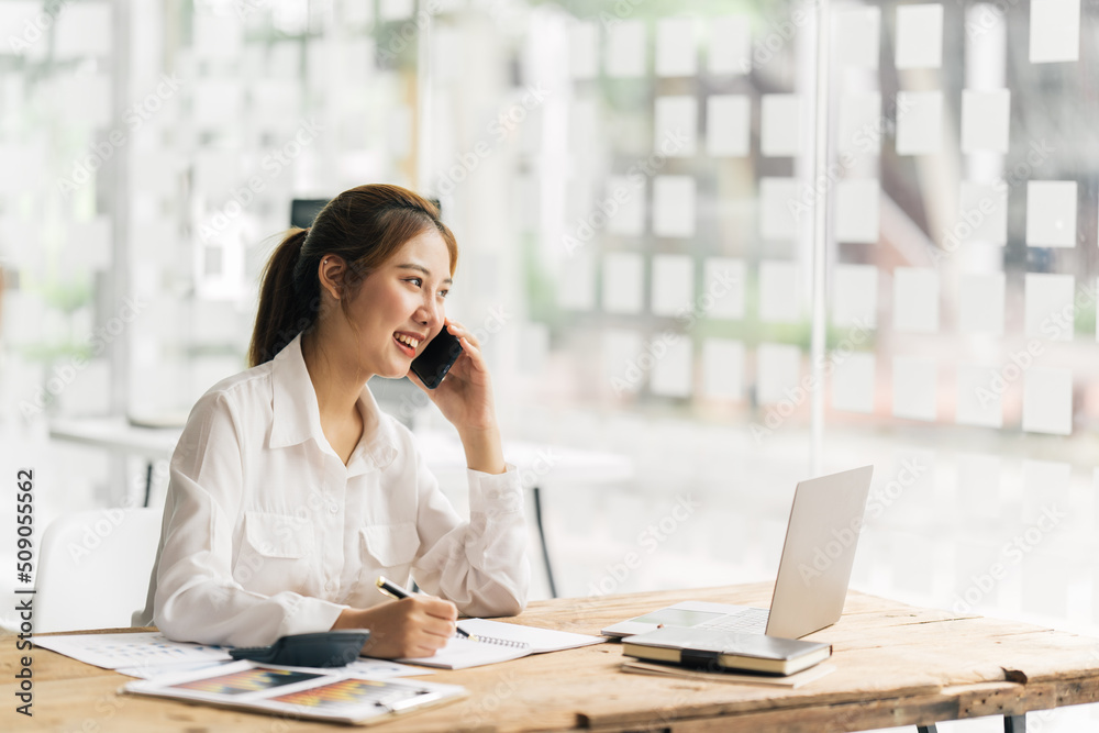 Asian woman using smart phone and laptop in office.