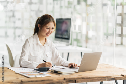 Happy attractive Asian business woman working with a laptop and financial document at office, successful action, Business concept.