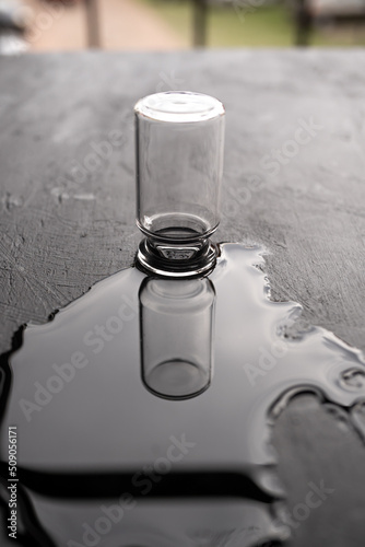 una botellita de vidrio y su reflejo en agua sobre madera negra con textura photo