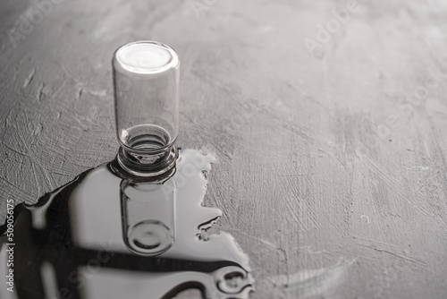 una botellita de vidrio y su reflejo en agua sobre madera negra con textura