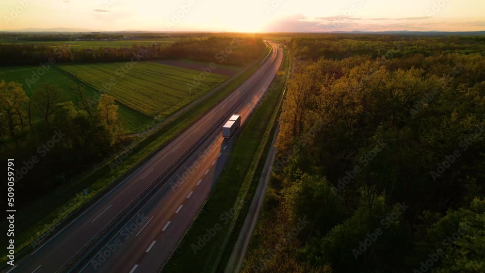 AERIAL: Convoy of cargo trucks on a countryside highway in beautiful golden light. Low traffic on a motorway that crosses beautiful landscape in gorgeous light. Truck transport for delivering goods.