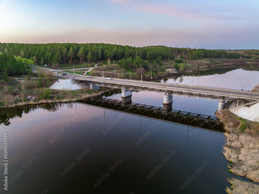 Obraz premium Beautiful view of the bridge across the Iset river in the city of Kamensk-Uralsky at sunset in spring. Kamensk-Uralskiy, Sverdlovsk region, Ural mountains, Russia.