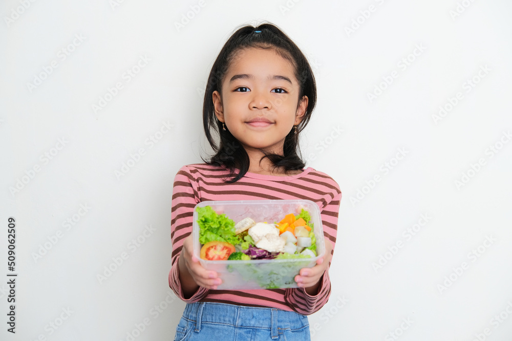 Asian little kid smiling to the camera while showing a box full of vegetables