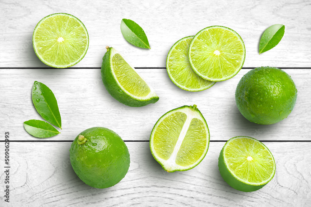 Whole and half sliced green lime with leaves isolated on grey wooden table background. Top view. Flat lay.