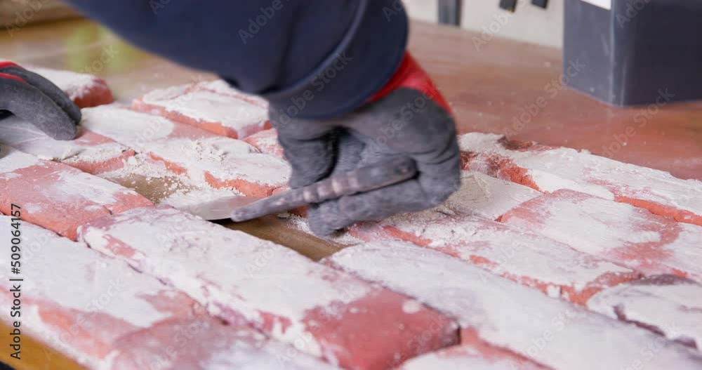 Man in rubber gloves removes plaster residue with spatula from old style orange brick casts on table at workshop. Handmade tile designed for facades closeup Man in rubber gloves removes plaster residue with spatula from old style orange brick casts on table at workshop. Handmade tile designed for facades closeup