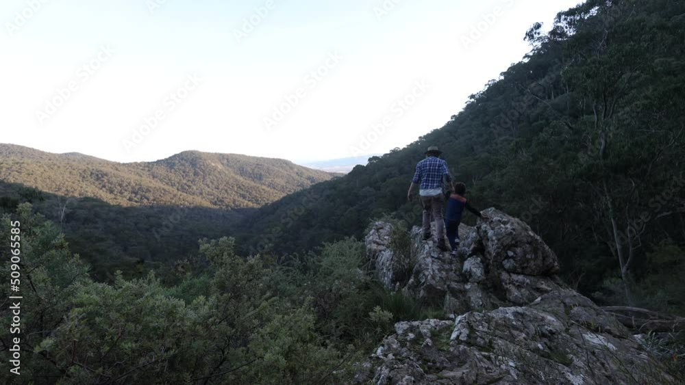 An Australian bushman and his son walking towards the edge of a craggy cliff looking out over the mountains. An Australian bushman and his son walking towards the edge of a craggy cliff looking out over the mountains.