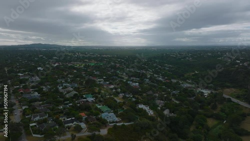 Aerial descending footage of residential neighbourhood on city outskirts. Family houses surrounded by green vegetation on cloudy day. Port Elisabeth, South Africa