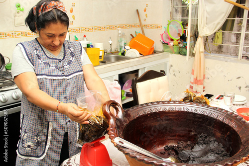 Latin Mexican adult woman prepares packages of freshly made red mole in clay pot to sell and follow the tradition and culture of the Mexican people
 photo