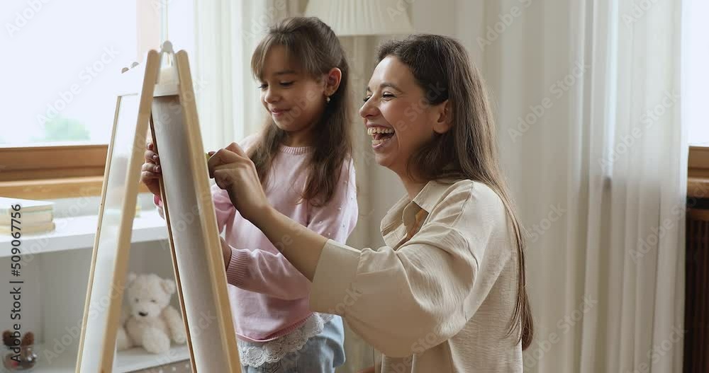 Little daughter and young loving mother drawing on white board with colored chalks at home. Take painting class for talent and skills development, creative hobby, art therapy with professional concept