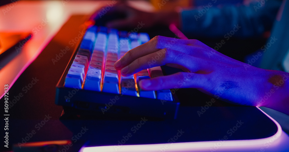 Close-up hands shot asia guy gamer use keyboard and mouse controller play video game with neon light computer in desk at home. Online esport streaming game online, Home quarantine activity concept.