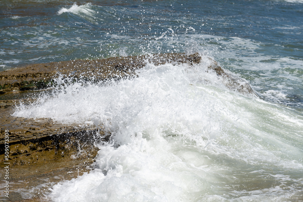 Splash wave rolls over ocean rocks
