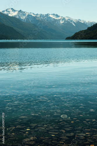 Obraz na płótnie Stones in a translucent lake with a snowy mountain range in the background. Vertical. Los Alerces National Park w salonie