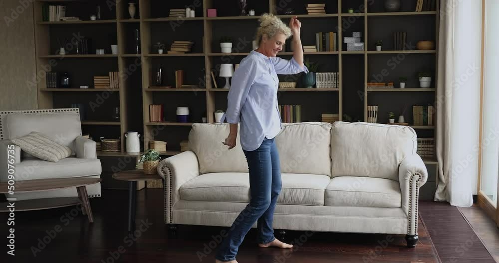 Active mature woman dancing in living room. Single senior lady listen favourite song moving to music looking happy enjoy comfort retired life at own modern dwelling. Leisure, no stress, hobby concept