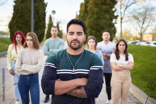 Latin man looking seriously at the camera while standing in front of a group of people. Concept of team and leadership.