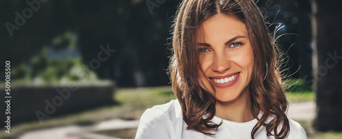 Portrait of a young cute girl in a white T-shirt with a smile in the park. Attractive girl smiling in the park and looking at the camera