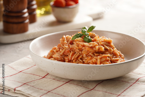 Homemade italian dish pasta risoni with tomato basil sauce in a deep bowl on checkered napkin photo