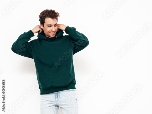 Handsome smiling hipster  model.Sexy unshaven man dressed in summer stylish green hoodie clothes. Fashion male with curly hairstyle posing in studio. Isolated on white