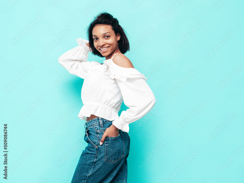 Portrait of young beautiful black woman. Smiling model dressed in summer jeans clothes. Sexy carefree female posing near blue wall in studio. Tanned and cheerful Portrait of young beautiful black woman. Smiling model dressed in summer jeans clothes. Sexy carefree female posing near blue wall in studio. Tanned and cheerful