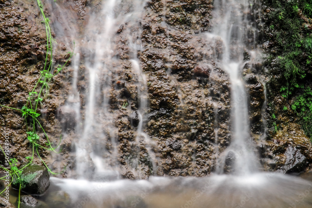 Obraz premium Beautiful waterfall in tropical green tree forest. Waterfall is flowing in jungle. Nature abstract background. Granite rock mountain
