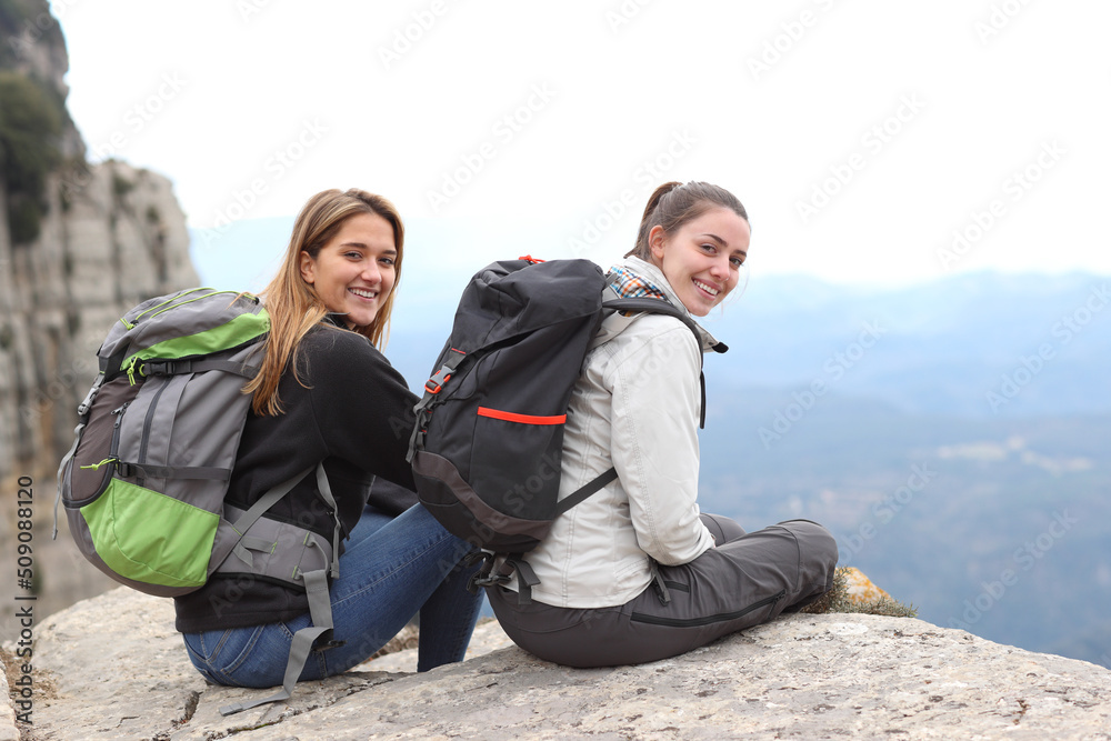 Happy trekkers sitting on top of a cliff looking at you