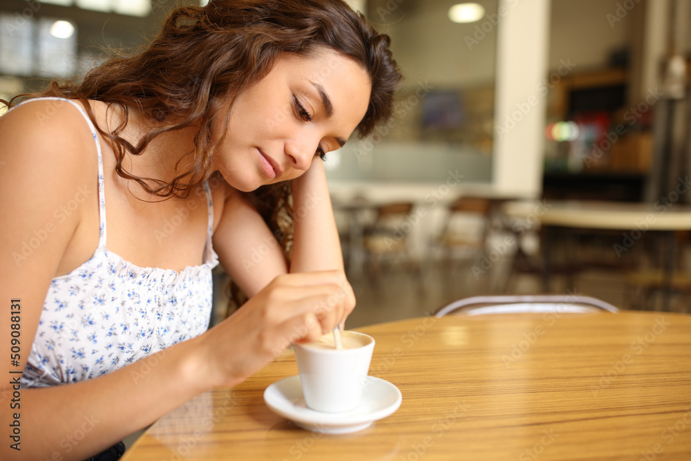 Pensive woman stirring coffee sitting in a restaurant Pensive woman stirring coffee sitting in a restaurant