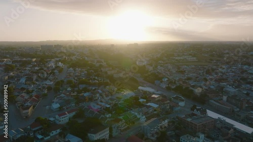 Fly above city at dusk. Residential buildings and streets in urban borough against setting sun. Port Elisabeth, South Africa