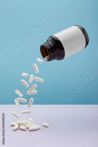 Capsules pouring out of a levitating jar with an empty label on a blue background.