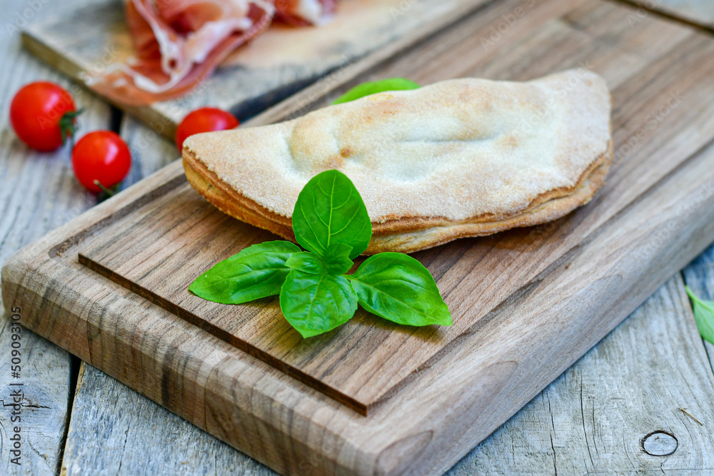 Home made italian calzone pizza with tomatoes, prosciutto mozzarella and parmesan cheese and fresh basil Home made italian calzone pizza with tomatoes, prosciutto mozzarella and parmesan cheese and fresh basil