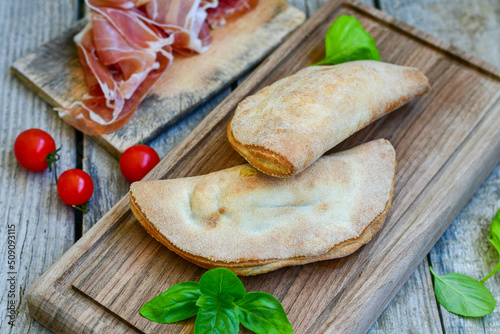 Home made italian calzone pizza with tomatoes, prosciutto mozzarella and parmesan cheese and fresh basil 