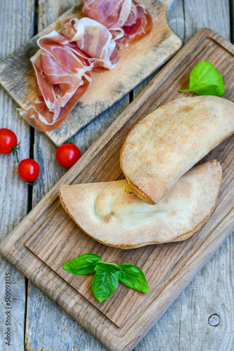 Home made italian calzone pizza with  tomatoes,  prosciutto mozzarella and parmesan cheese and fresh basil 
