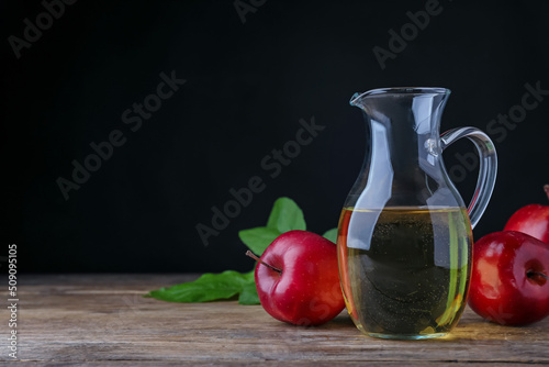 Jug of tasty juice and fresh red apples on wooden table against black background, space for text photo