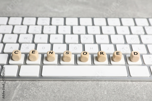 Wooden cubes with word Censored and keyboard on light grey table, closeup photo