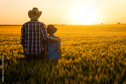 Foto Father and son are standing in their growing wheat field