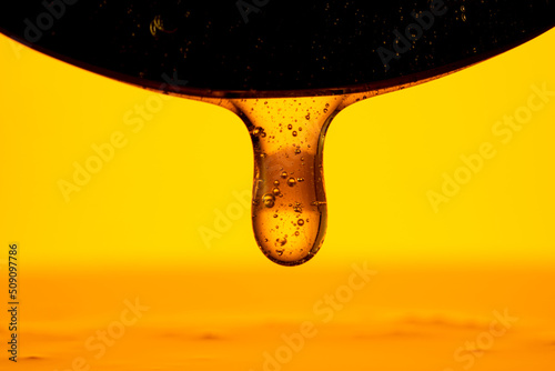 Schilderij op canvas Thick drops of honey flowing down from a dark black spoon on yellow background