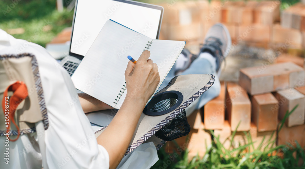 Fototapeta premium Casual asian woman sitting on folding chair she writing her job in book and working part time with laptop and relax on summer camp