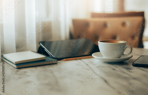 Close up view, white coffee cup with digital tablet, notebook and smart phone on table in cafe near bright window, Vintage color tone, Concept holiday and relax after work