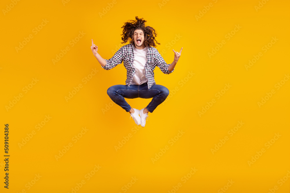 Full size photo of young excited guy jump up show fingers rock metal party swag symbol isolated over yellow color background