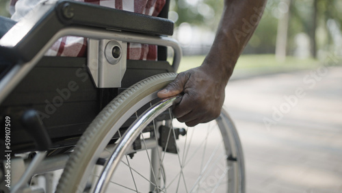 Hands of black man pushing wheel of wheelchair, life with disability in a city