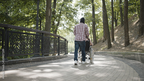 Photos Back view of young man taking care of relative with disability, pushing wheelcha