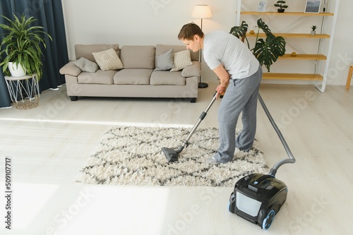 Portrait of senior woman with vacuum cleaner indoors at home, hoovering