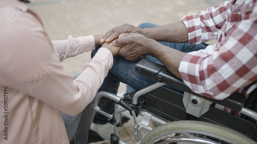 Woman and man in wheelchair holding hands, love and support in a relationship