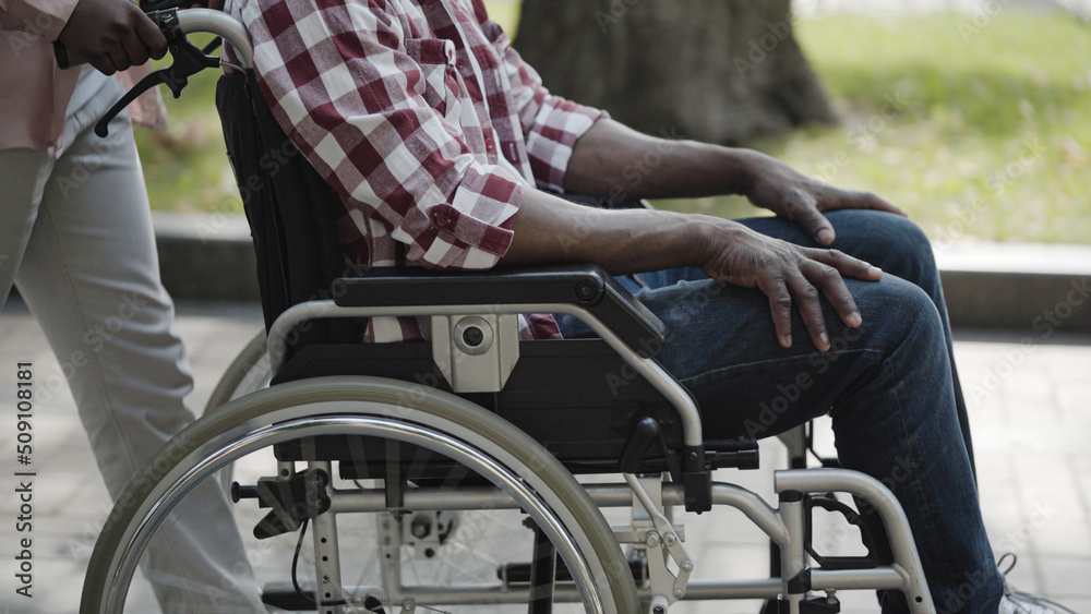 Obraz premium Nurse pushing wheelchair of man with disability outdoors, taking care of patient, close-up