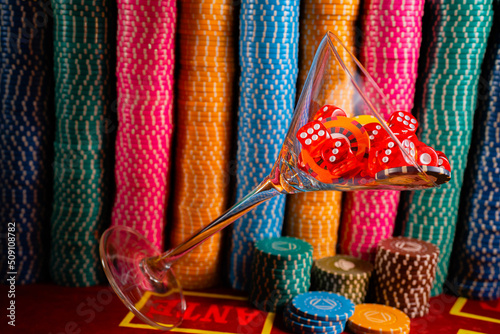 A set of red dice and chips in a falling martin glass on the background of casino chips. Close up of casino chips and dice. Gambling background. Poker, roulette, blackjack. Betting, risk, success.