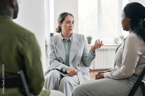 Modern young psychotherapist communicating with African American female patient while sitting in front of her during session