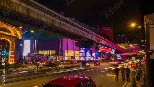 Timelapse of modern Asian city intersection at night. Car light trails, urban lights, ads, people cross streets, monorail train station, Kuala Lumpur