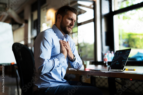 Young businessman having chest pain. Man sitting in the office working on laptop..
