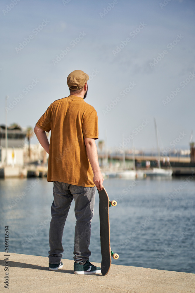 an unrecognizable person standing with his skateboard in his hand looking out to sea